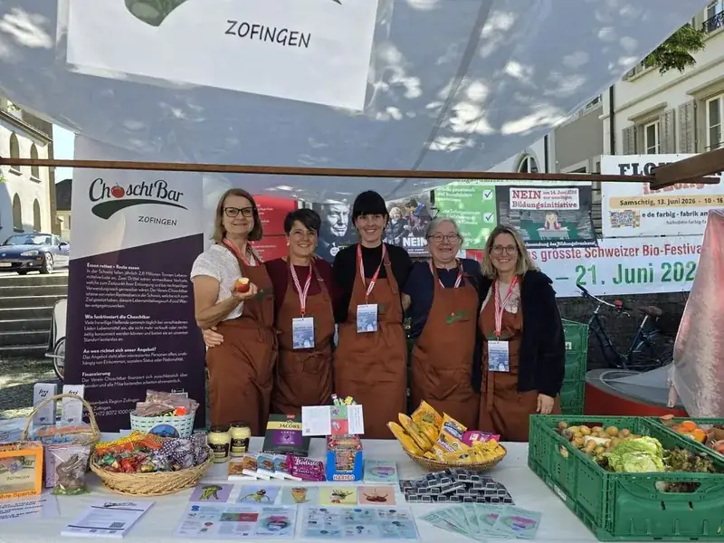 Freiwillige der ChoschtBar Zofingen an einem Informationsstand mit Logo-Banner an einem Markt