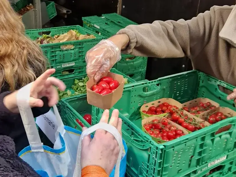 Freiwillige übergibt einer Besucherin frisch geerntete Cherrytomaten, im Hintergrund Kisten mit weiterem geretteten Gemüse