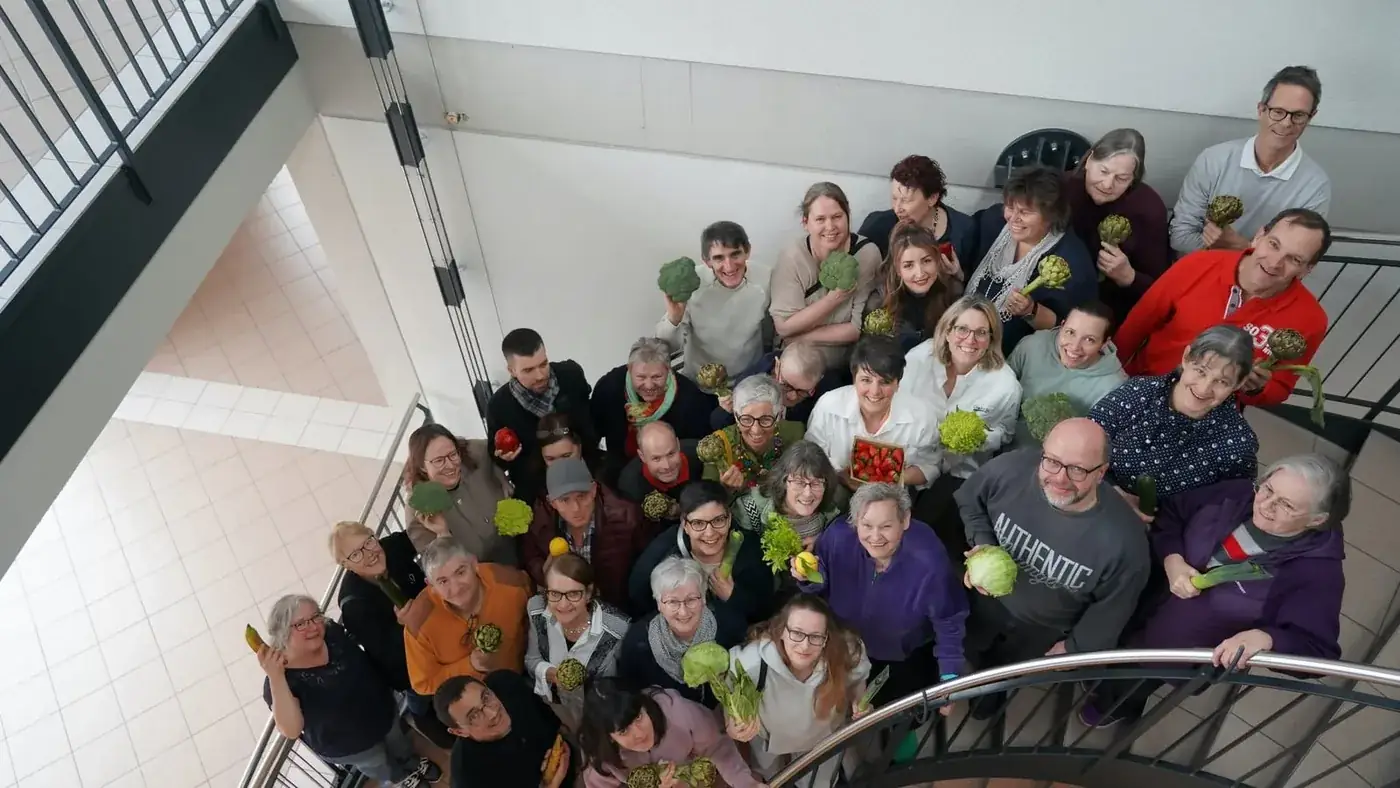 Grosse Gruppe von Freiwilligen der ChoschtBar Zofingen auf einer Wendeltreppe von oben fotografiert, jede und jeder hält ein gerettetes Gemüse in der Hand